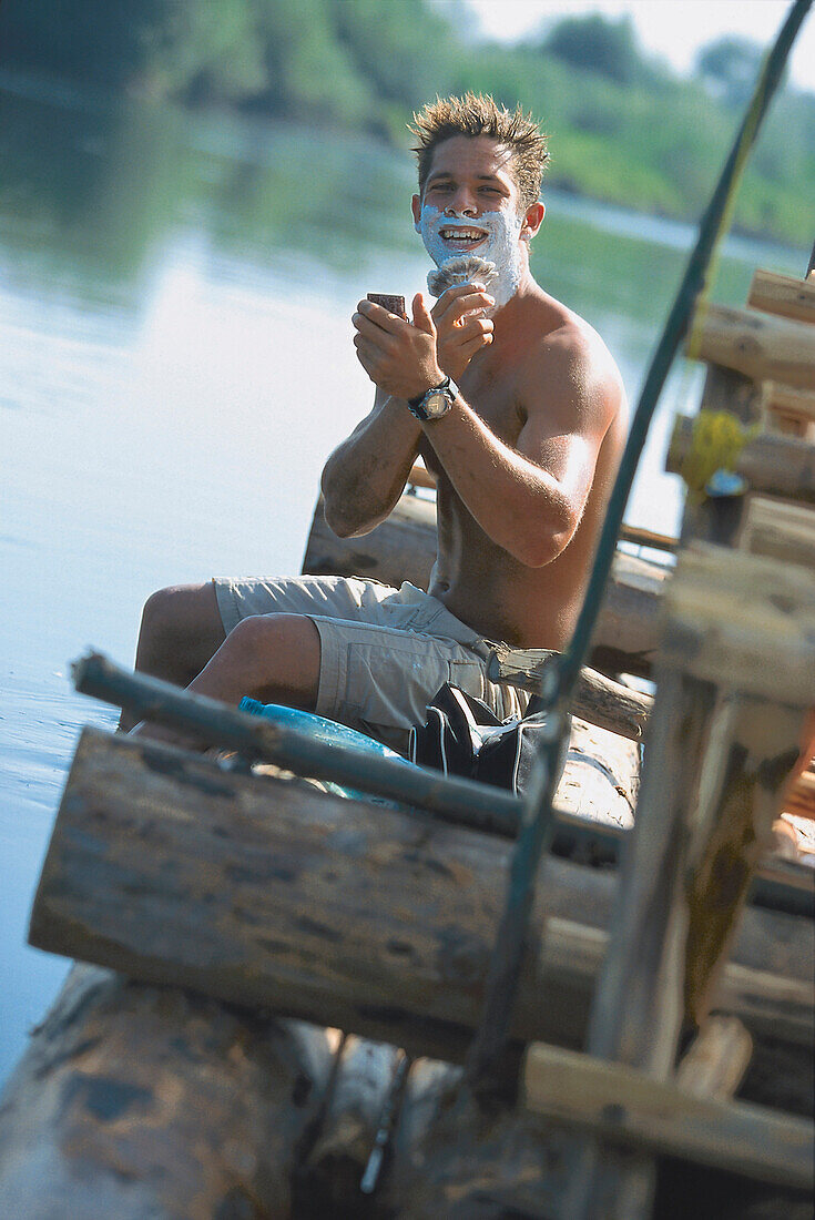 Mann sitzt auf einem Floß und rasiert sich