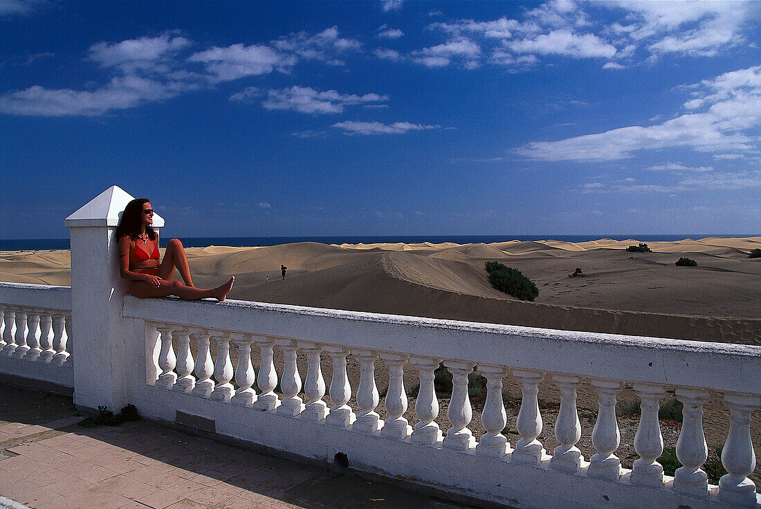 Young woman sitting on railing overlooking Maspalomas, Gran Canaria, Spain