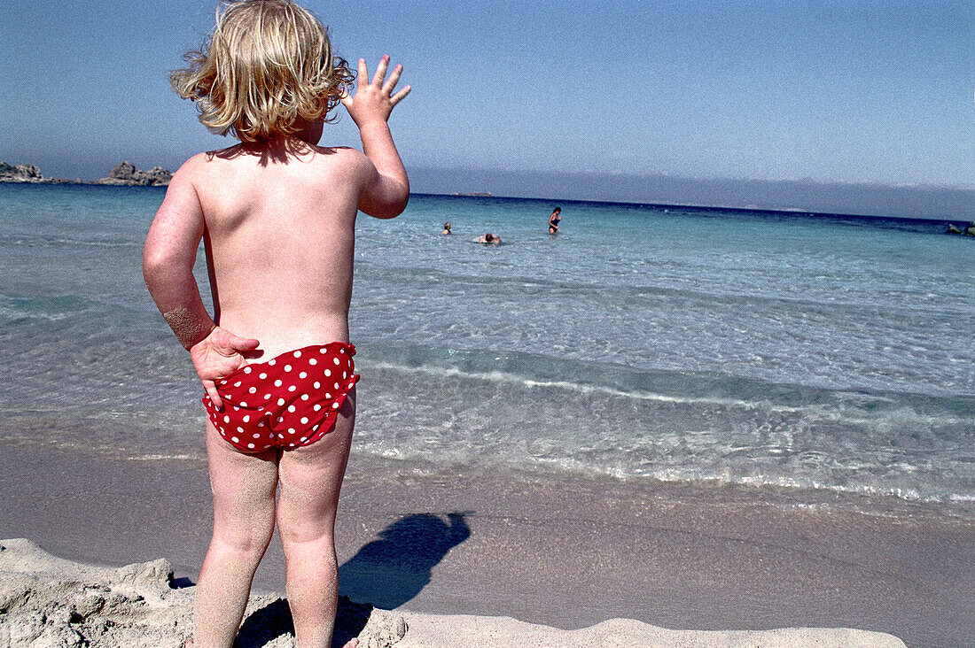 Kleines Kind steht am Strand in der Sonne, Sardinien, Italien