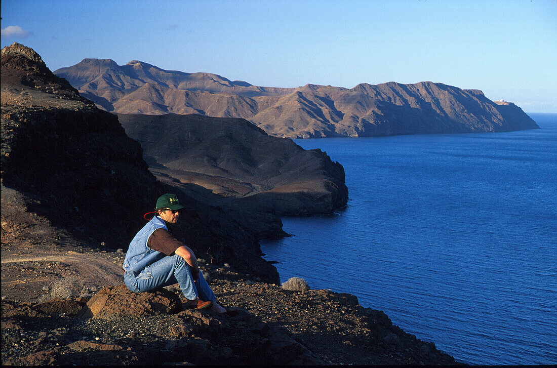 Mann sitzt oberhalb einer Steilküste, Fuerteventura, Kanarische Inseln, Spanien, Europa
