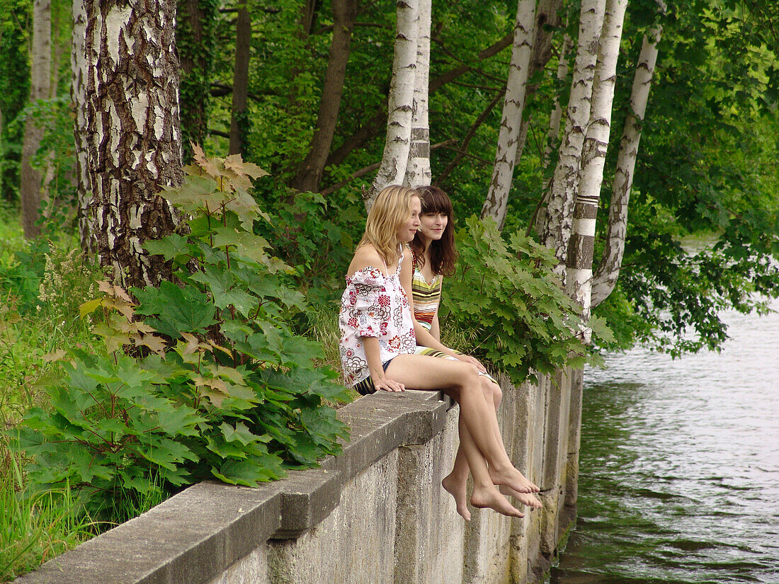 Two young women sitting at Spree River, Berlin, Germany