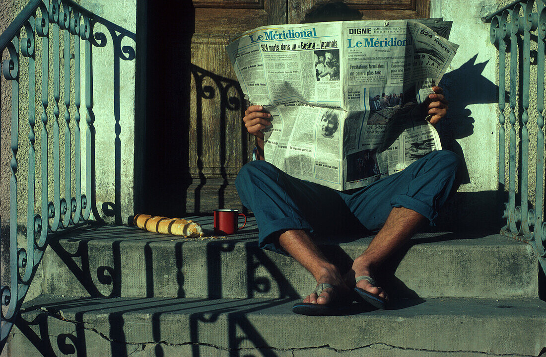 Französisches Frühstück, Mann liest Zeitung auf einer Treppe