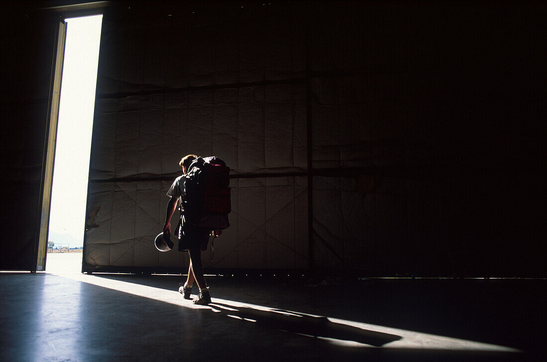 Fallschirmspringer geht durch eine Halle hinaus in die Freiheit, Rucksack, Stiefel und Helm