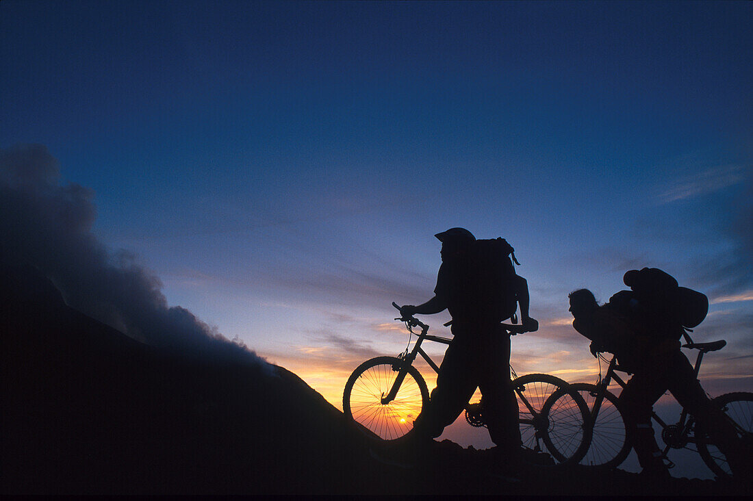 Two mountain bikers against sunset, Vulcano, Liparian Islands, Italy