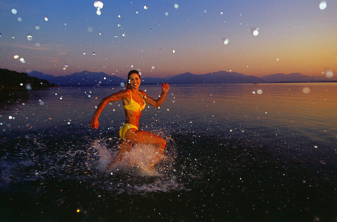 Woman running into water of Lake Chiemsee, Upper Bavaria, Germany