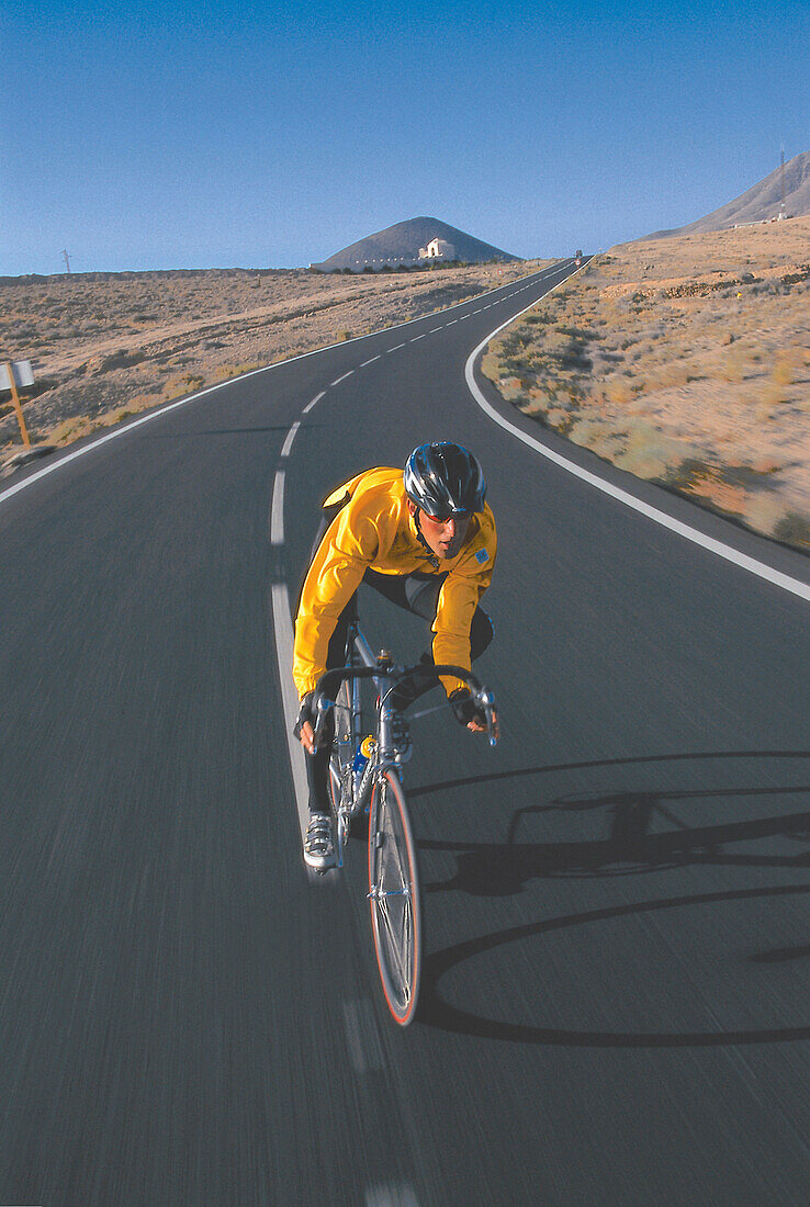 Rennradfahrer fährt entlang der Landstrasse, Fuerteventura, Kanarische Inseln, Spanien