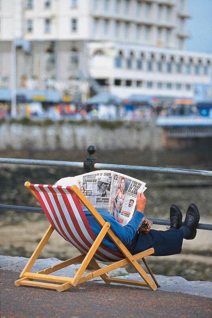 Mann liest Zeitung in einem Liegestuhl, Llandudno, Gwynedd, Wales, Großbritannien