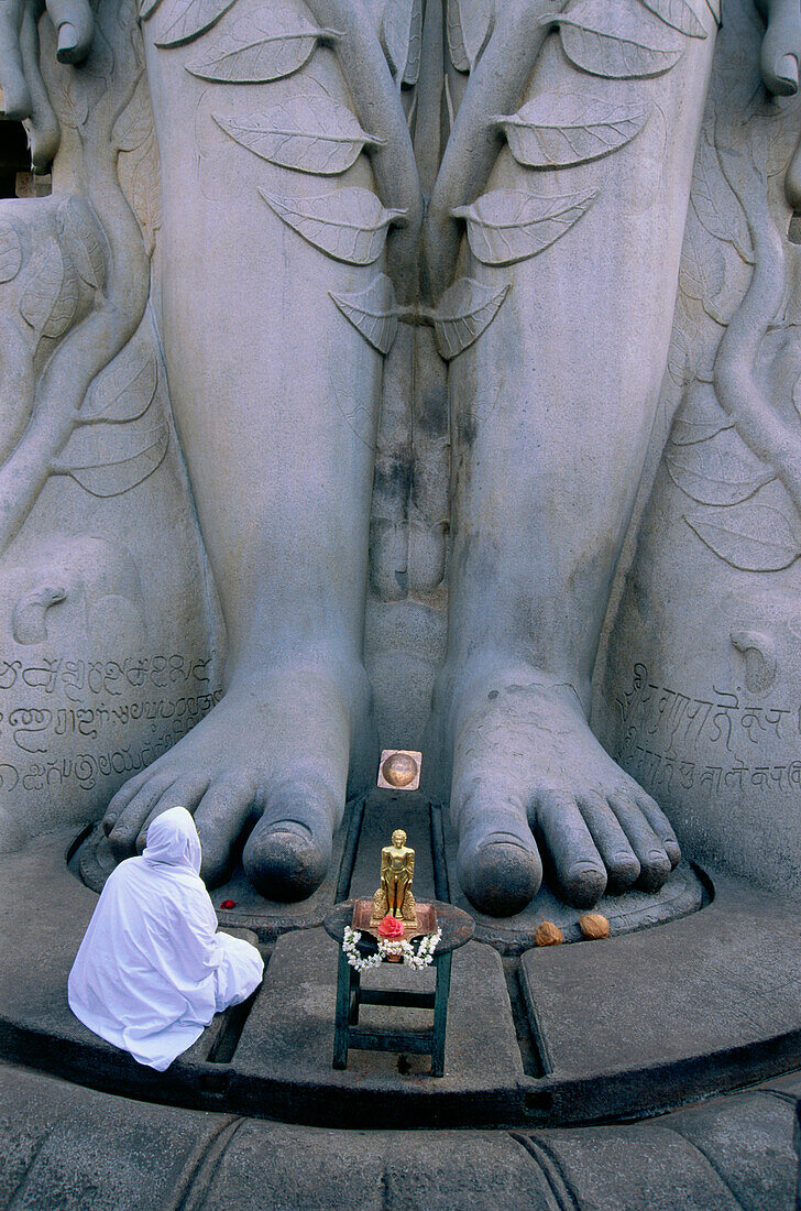 Eine Person hockt vor den Füsse der riesigen Sri Gometeshwara Statue, Sravanabelagola, Karnataka, Indien