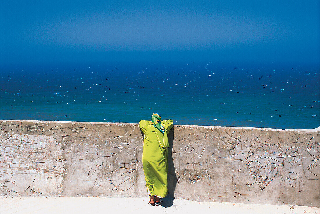 Frau lehnt an einer Mauer und blickt aufs Meer, Medina, Tanger, Marokko, Afrika