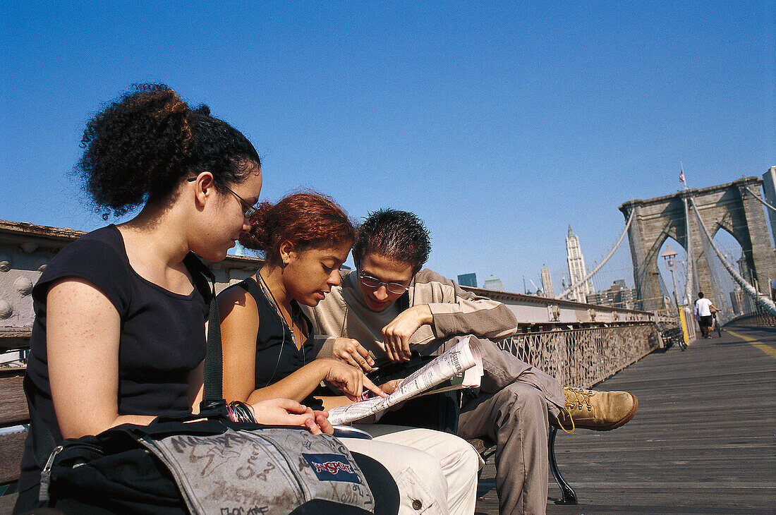 People sitting on Brooklyn Bridge in the sunlight, Manhattan, New York, USA, America