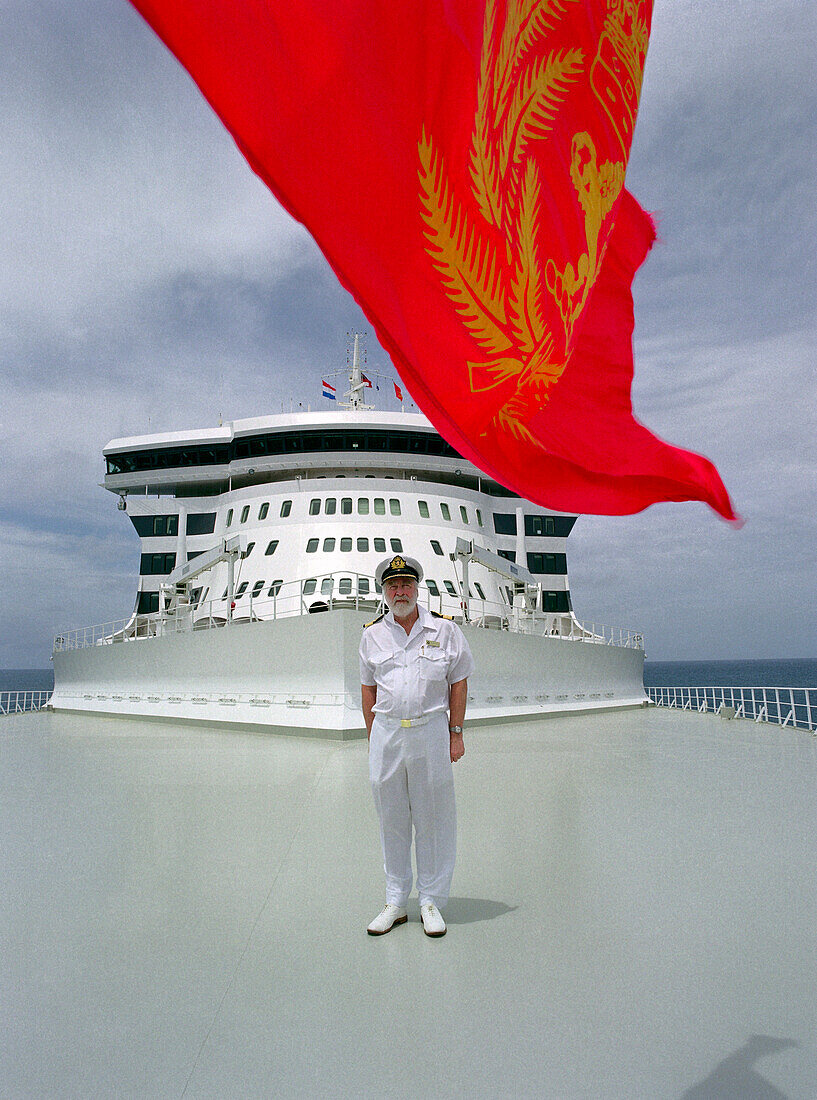 Kapitän Ronald Warwick steht auf dem Deck unter einer roten Flagge, Kreuzfahrtschiff Queen Mary 2