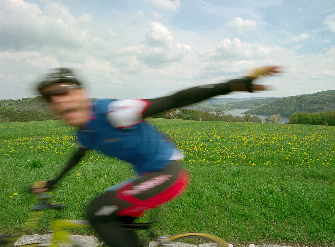 Biker on racing bike near Rurtalsperre reservoir, Eifel, North Rhine-Westphalia, Germany