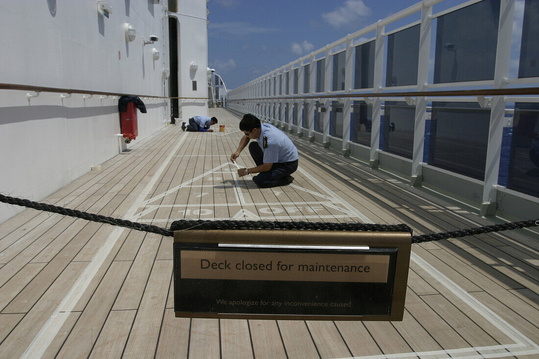 Queen Mary2-Painting figures for shuffleboard game, Queen Mary 2, QM2 Besatzungsangehoerige malen die Zahlen des Shuffleboard Spieles mit weisser Farbe nach. Deck 12. Buch S. 147