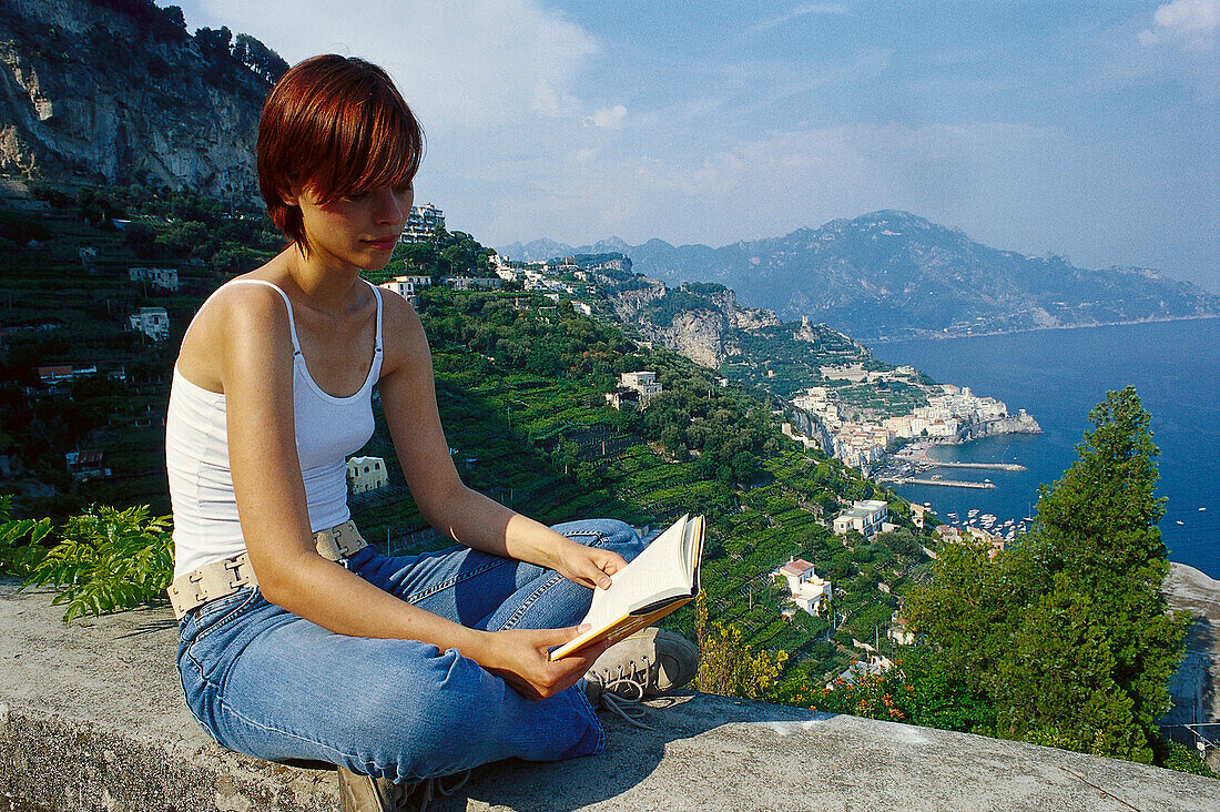 Junge frau liest ein Buch auf einer Mauer, Conca dei Marini, Amalfi, Campania, Italien, Europa