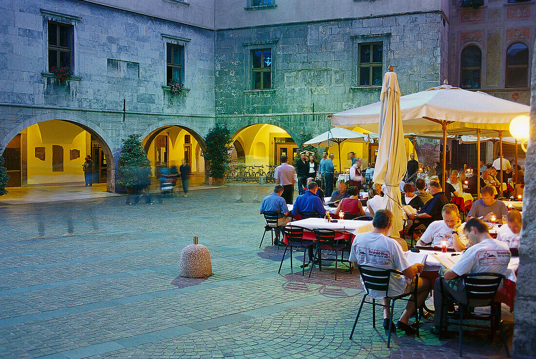 Menschen sitzen an Tischen eines Restaurants auf der Piazza Tre Novembre am Abend, Riva del Garda, Gardasee, Trentino, Italien, Europa