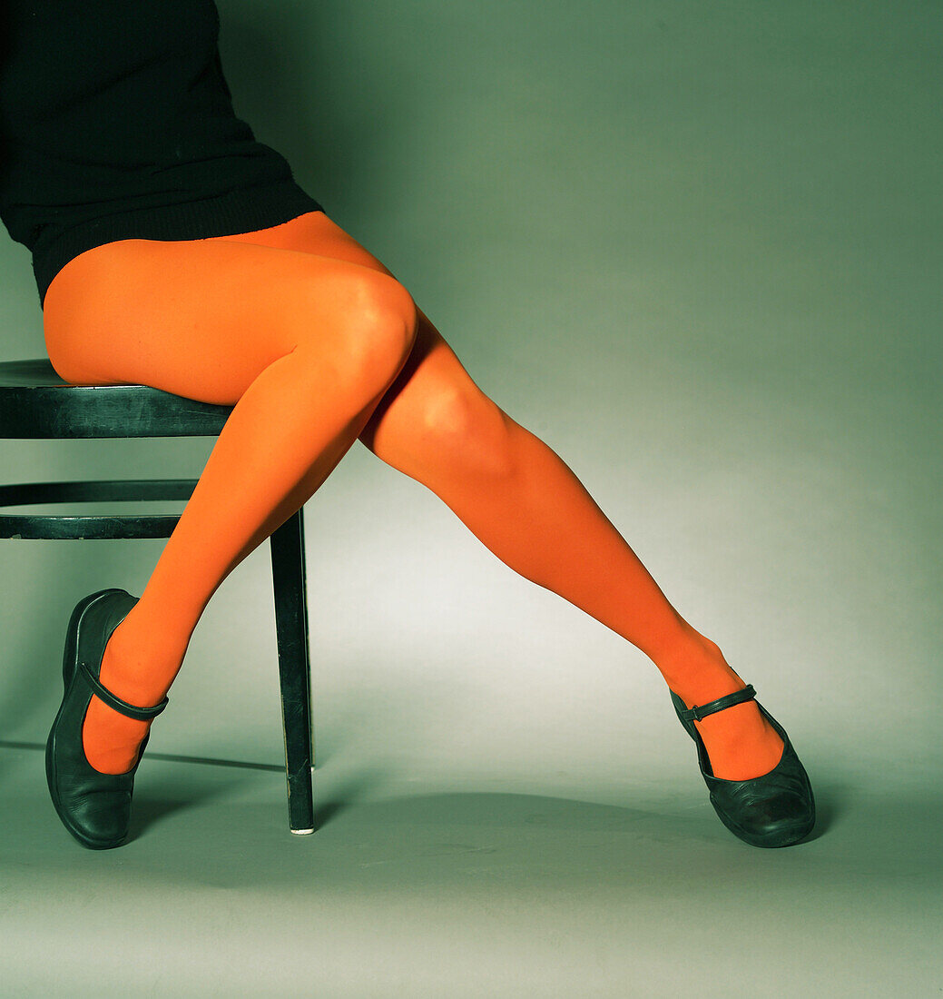 Eine junge Frau sitzt und zeigt Ihre Beine in roter Strumpfhose mit schwarzen Ballerinas