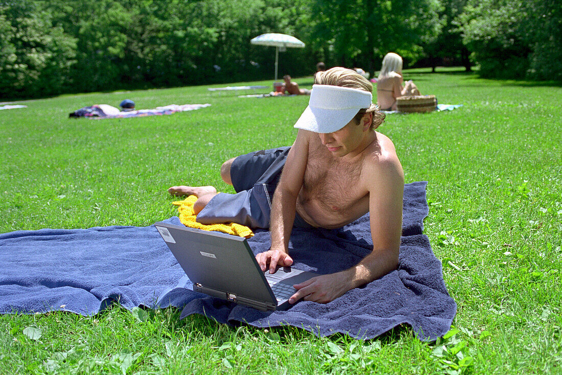 Youn man with laptop on meadow, Starnberg lake, Bavaria, Germany