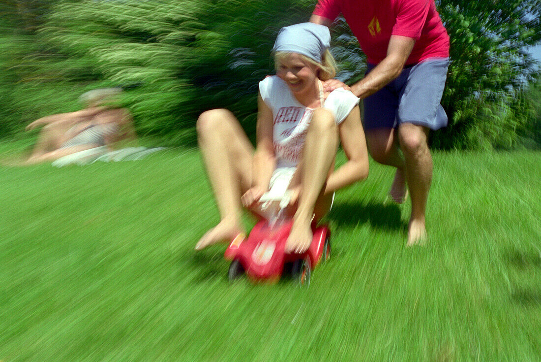 Young man pushing young woman on a toy car