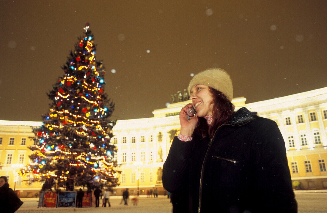 Christmas tree and woman with cell phone on Palace Square at night, St. Petersburg, Russia, Europe