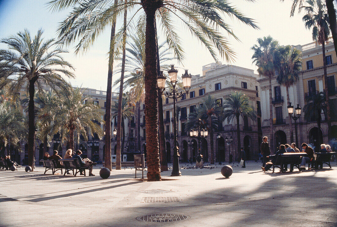 Menschen sitzen auf Bänken in der Sonne, Placa Real, Barcelona, Spanien