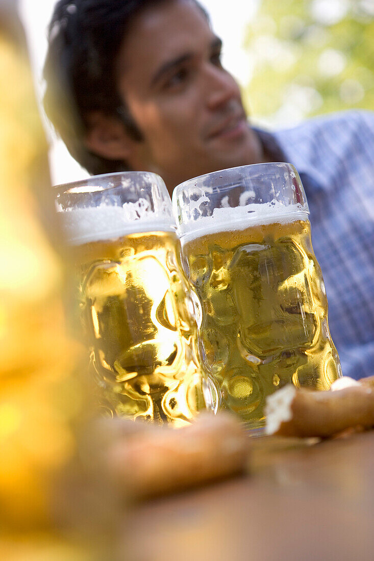 Three beer steins against face of young man, Munich, Bavaria