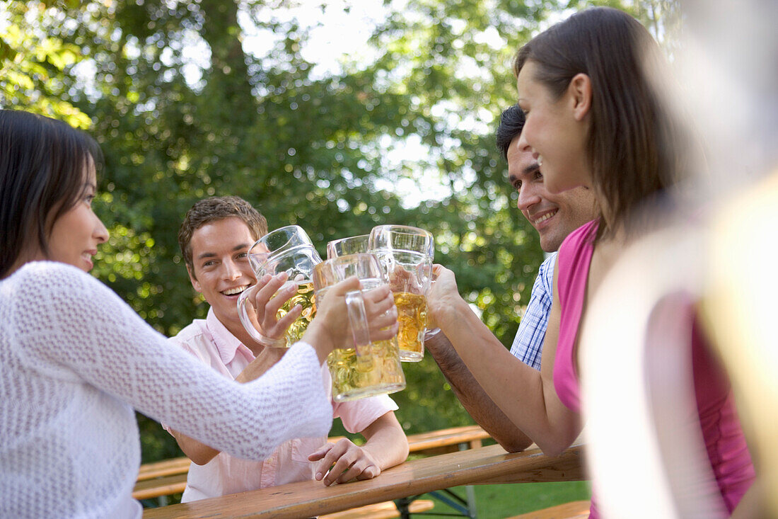 Four young people toasting each other in beer garden, Munich, Bavaria