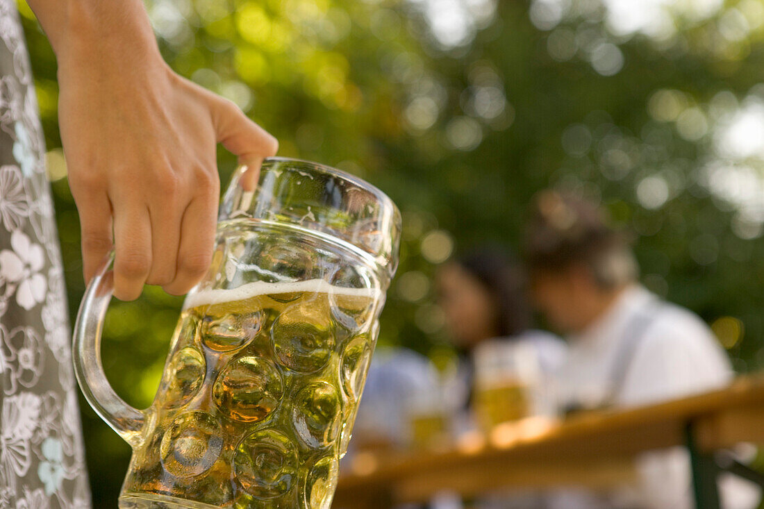 Female hand holding beer stein in beer garden, Munich, Bavaria