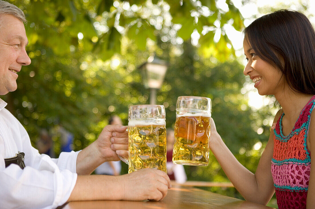 Older Bavarian man and asian woman toasting each other, Munich, Bavaria