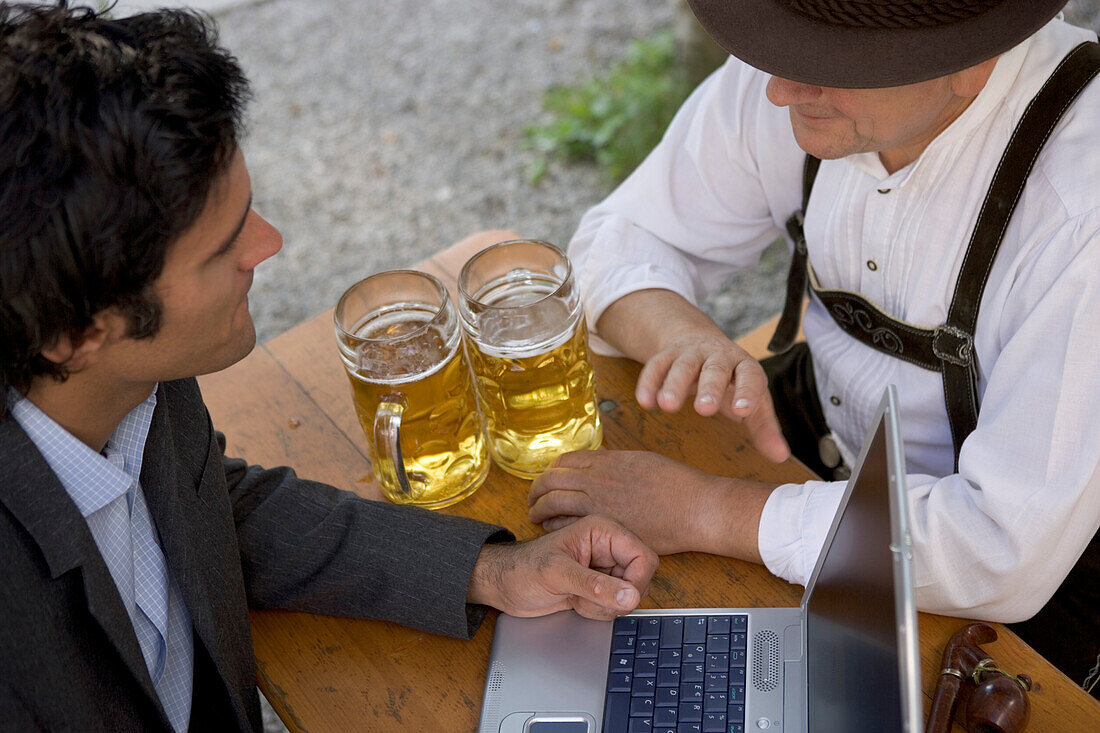 Young business man and older Bavarian man in beer garden, Munich, Bavaria