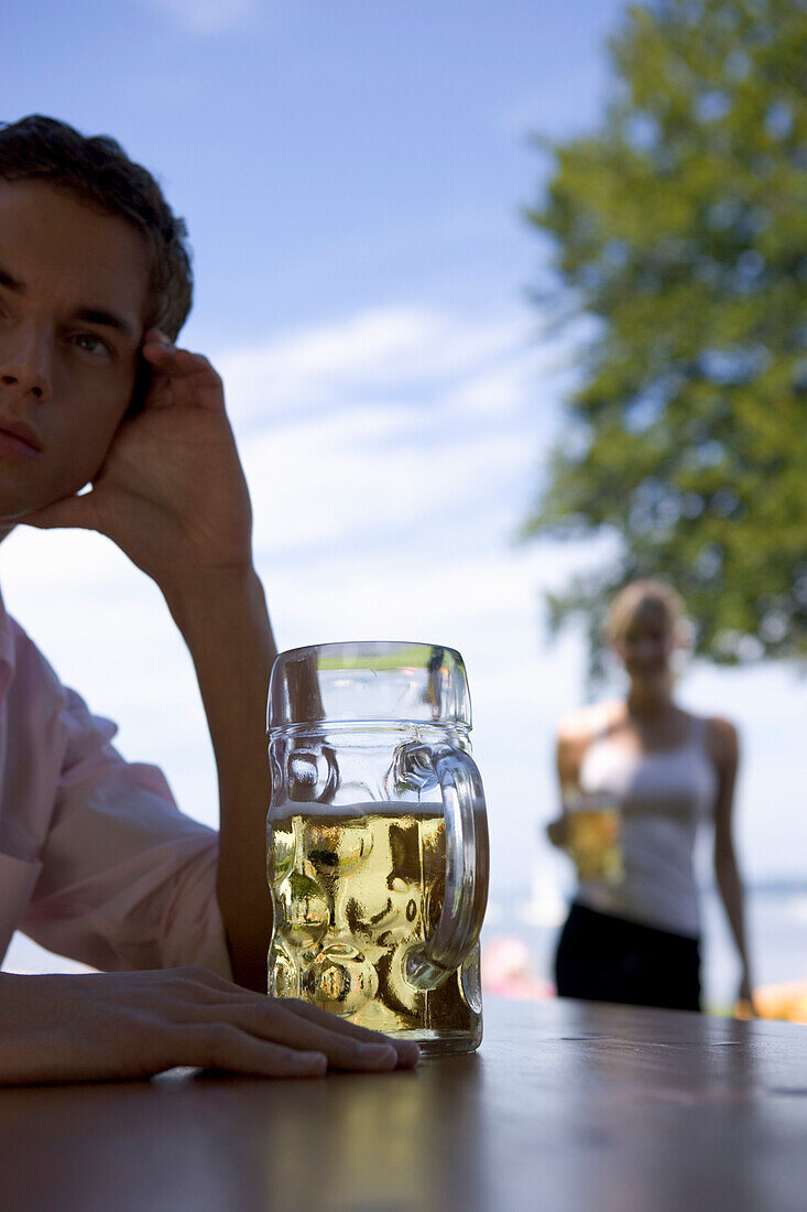 Junger Mann wartet auf jemand in Biergarten beim Starnberger See, Bayern, Deutschland