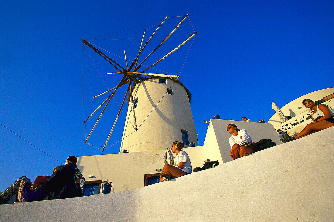 Menschen sitzen vor einer Windmühle im Sonnenlicht, Oia, Santorin, Griechenland, Europa