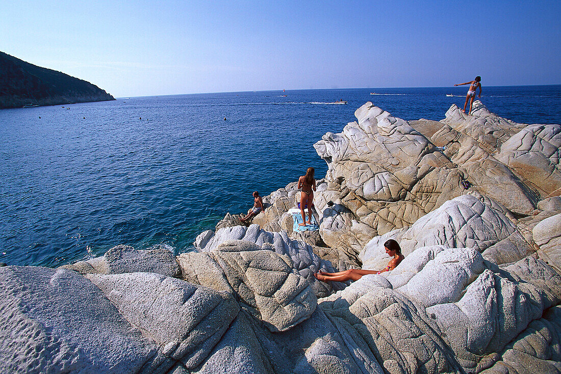 Menschen sitzen auf Steinen am Strand von Marciana Marina, Elba, Toskana, Italien, Europa