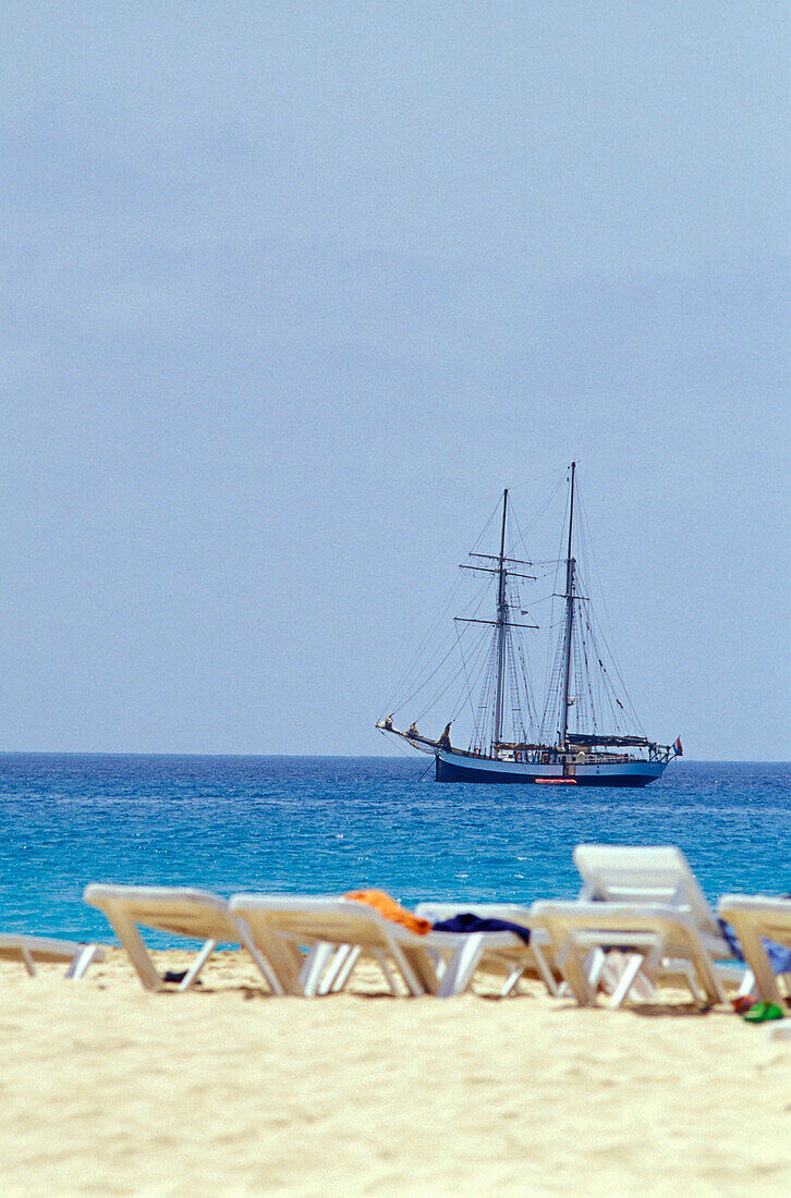 Sonnenliegen am Strand und Segelschiff im Meer, Santa Maria, Sal, Kap Verde, Afrika