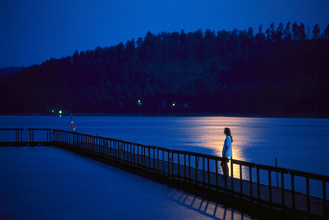 Woman standing on jetty, moonlight over Asunden Lake, Vastergotland, Sweden