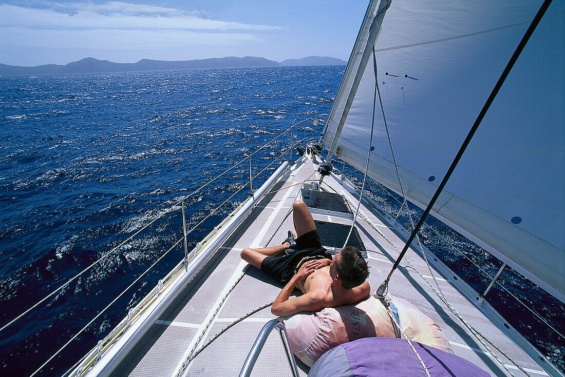 Ein Mann sonnt sich auf dem Bug eines Segelboots, Bequia, St. Vincent, Grenadinen, Karibik, Amerika