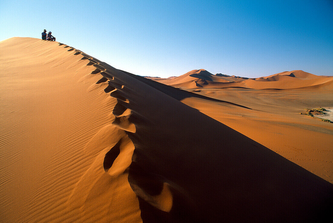 Touristen sitzen auf einer Sanddüne unter blauem Himmel, Sossusvlei, Namib, Naukluft Park, Namibia, Afrika