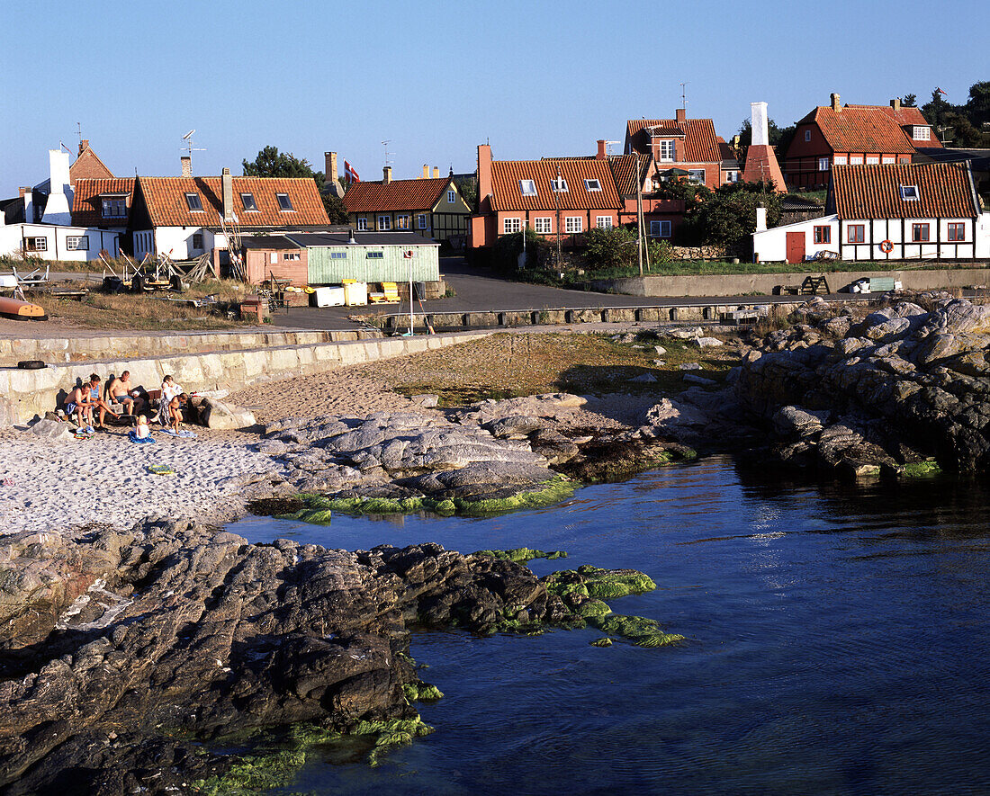 People at a pebbled beach and the houses of Gudhejm, North Coast, Bornholm Denmark