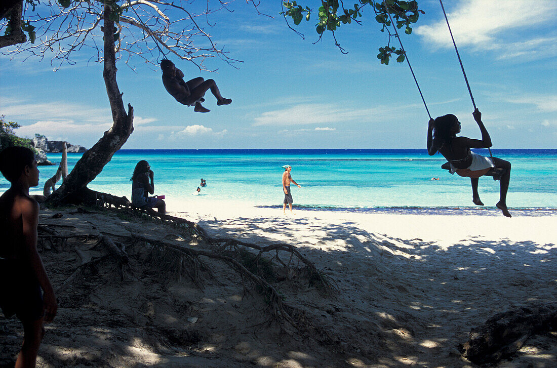 Kinder schaukeln an einem Strand im Schatten, Winnifred Bay, Port Antonio, Portland, Jamaika, Karibik, Amerika