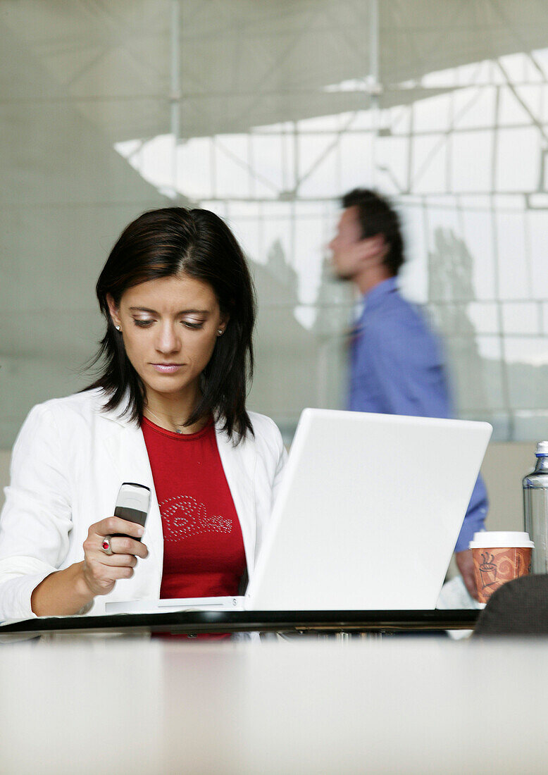 Geschäftsfrau arbeitet an einem Laptop, hält ein Handy in der Hand, Wien, Österreich
