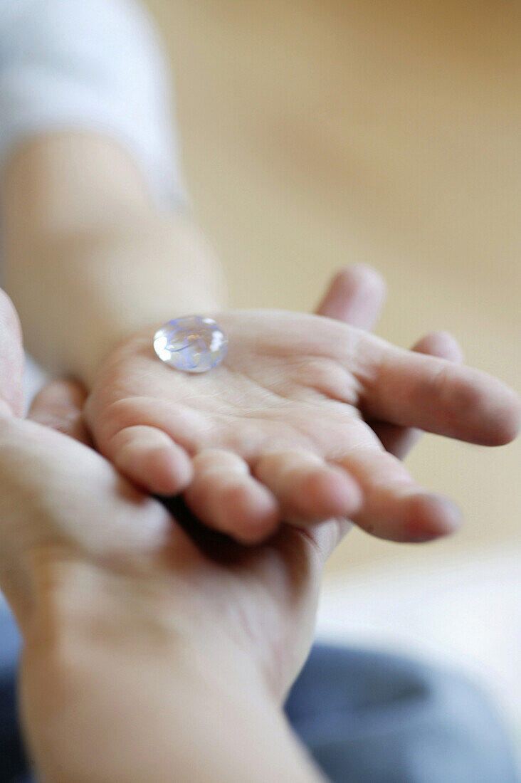 Kinderhand mit Glasstein auf Hand eines Erwachsenen, Wien, Österreich