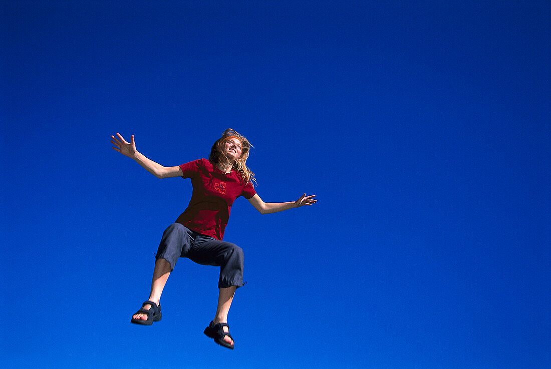 Woman jumping up in front of cloudless sky