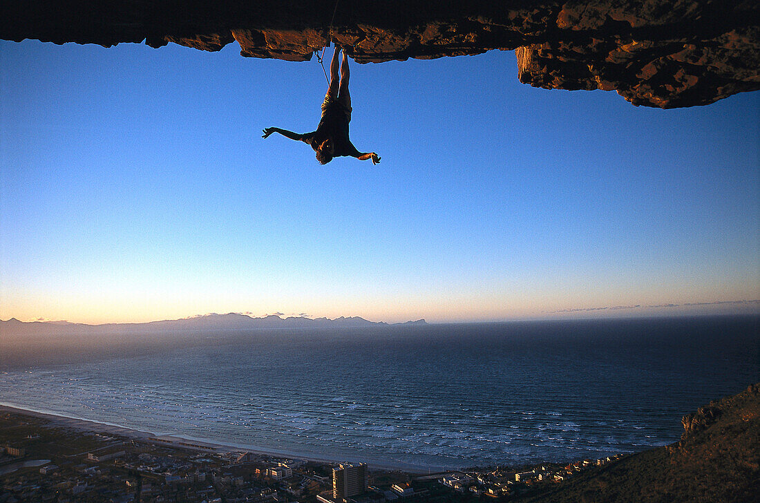 Rock climber hanging upside down, Muizenberg Bay, South Africa