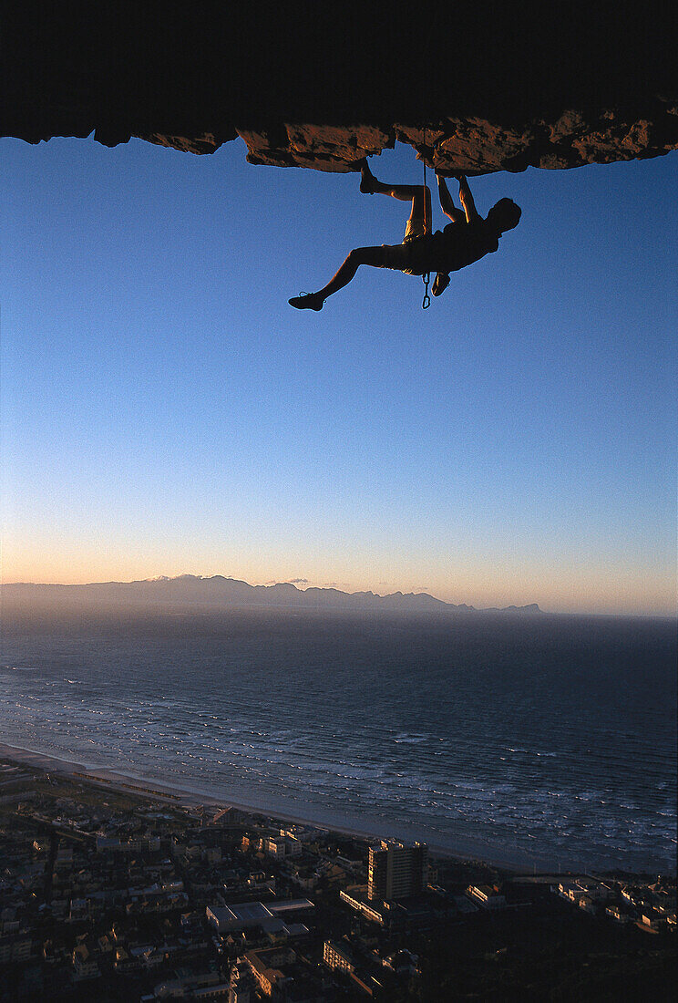 Rock climber climbing an overhang, Muizenberg Bay, South Africa