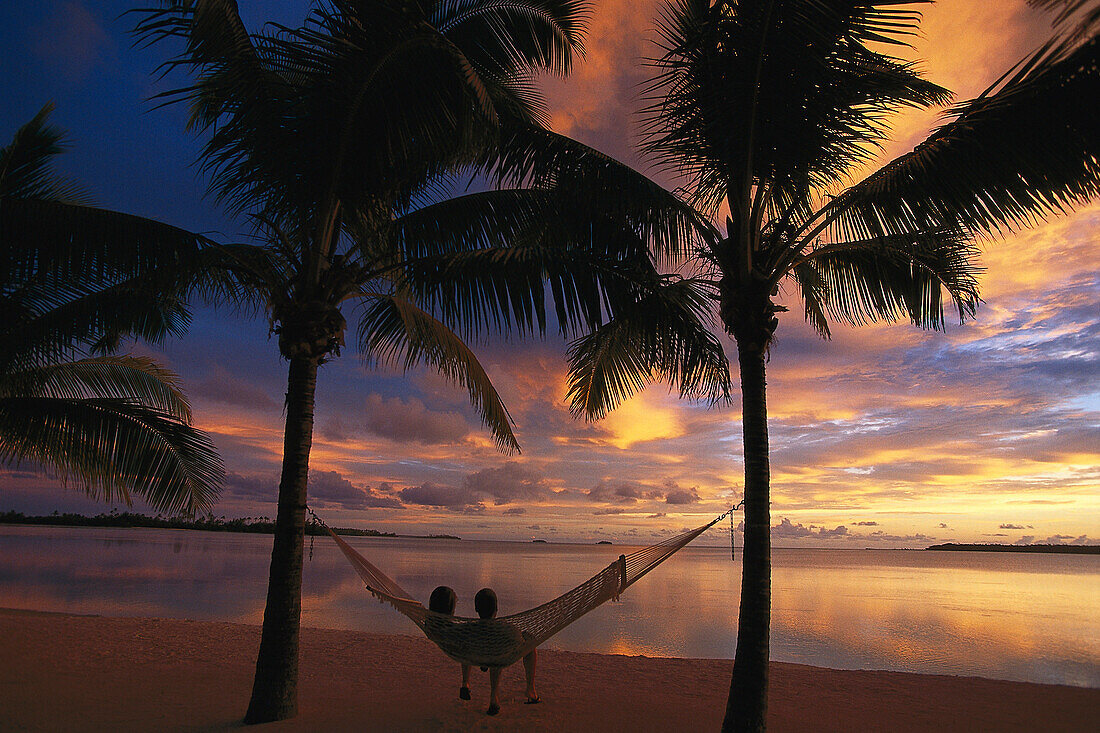 Paar entspannt sich in der Hängematte beim Sonnenuntergang, Aitutaki Lagoon Resort, Cook Islands, Südsee