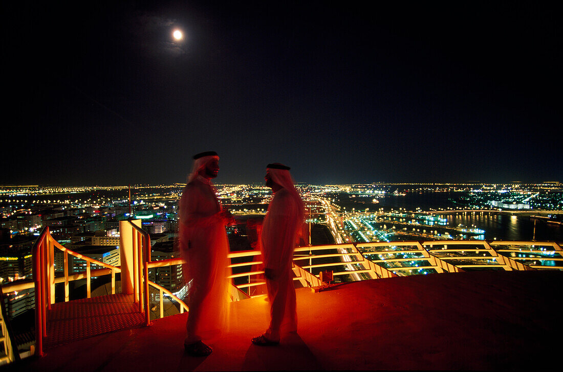 Two Arabs on a roof terrace at night, View towards Bur Deira, Dubai, United Arab Emirates, UAE