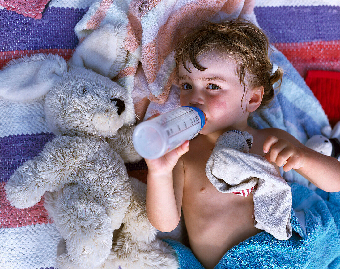 Child lying on blanket, drinking from baby bottle, Dueodde, Bornholm, Baltic Sea, Denmark