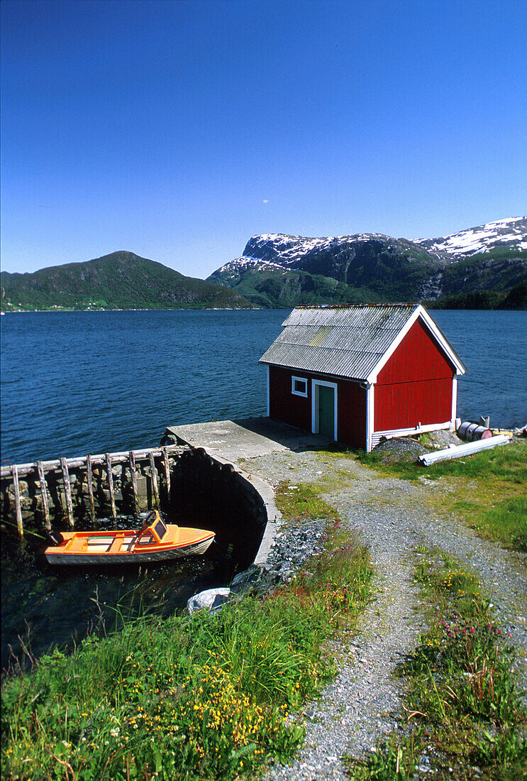 Holzhaus mit Bootssteg an einem Fjord im Sonnenlicht, Sogn og Fjordane, Norwegen, Europa