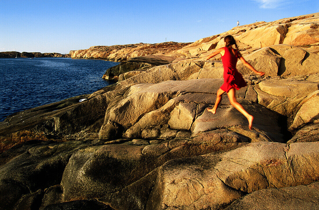 Woman jumping over rocks on coast, Bohuslan region, Vastra Gotaland, Sweden