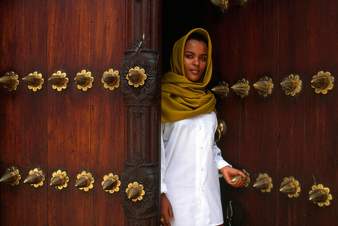 Moslem woman standing at an old door, Stone Town, Zanzibar City, Zanzbar, Tanzania