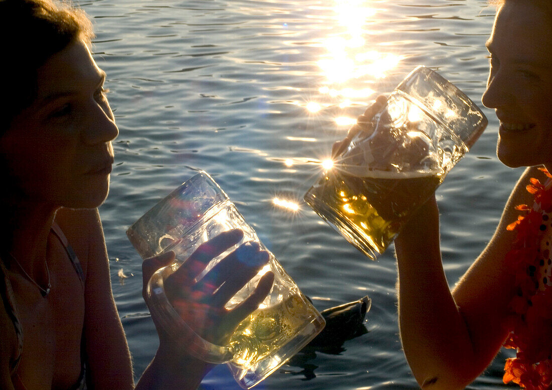 Junge Frauen stoßen mit Bier an, Biergarten Seehaus, Englischer Garten, München, Bayern, Deutschland
